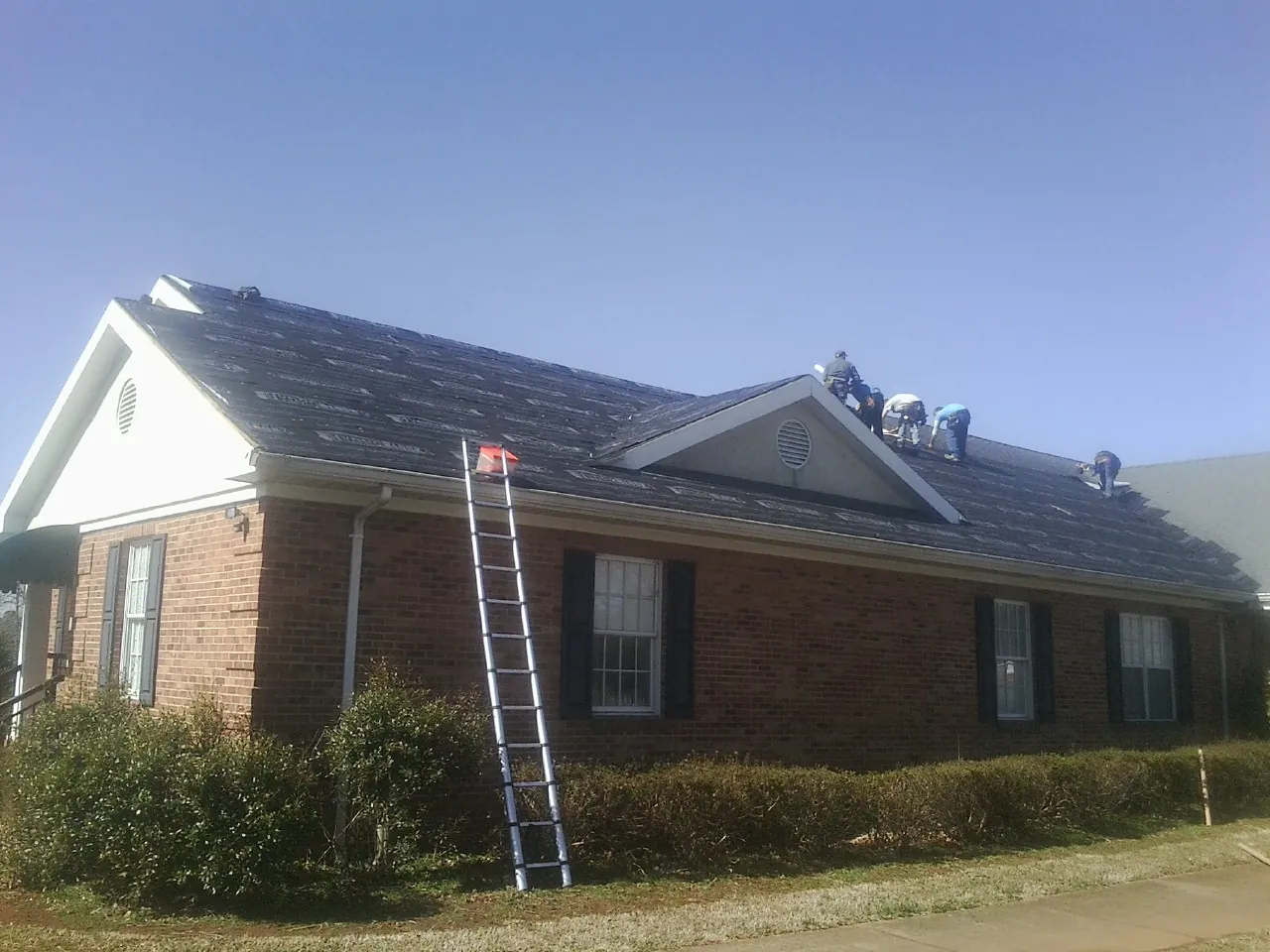 Crew tearing shingles off a brick ranch roof with a ladder set — Metal Roof Repair work by our crew in Bala Cynwyd