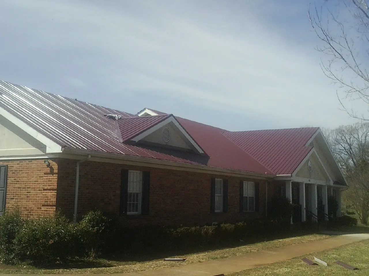 Red metal roof with gabled entries on a long brick building, from a Hail Damage Roof Repair job in Bala Cynwyd