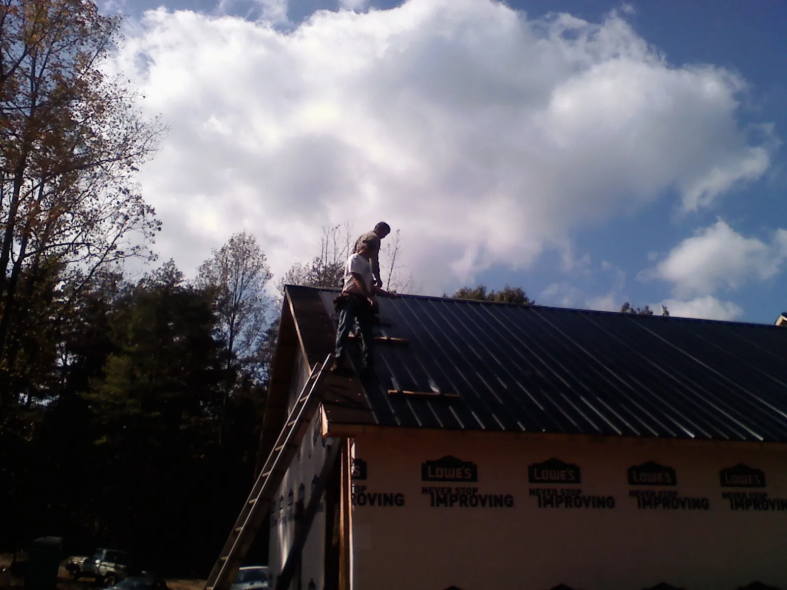 Roofer fastening dark metal panels high against a cloudy sky, from a Roof Inspection job in Bala Cynwyd