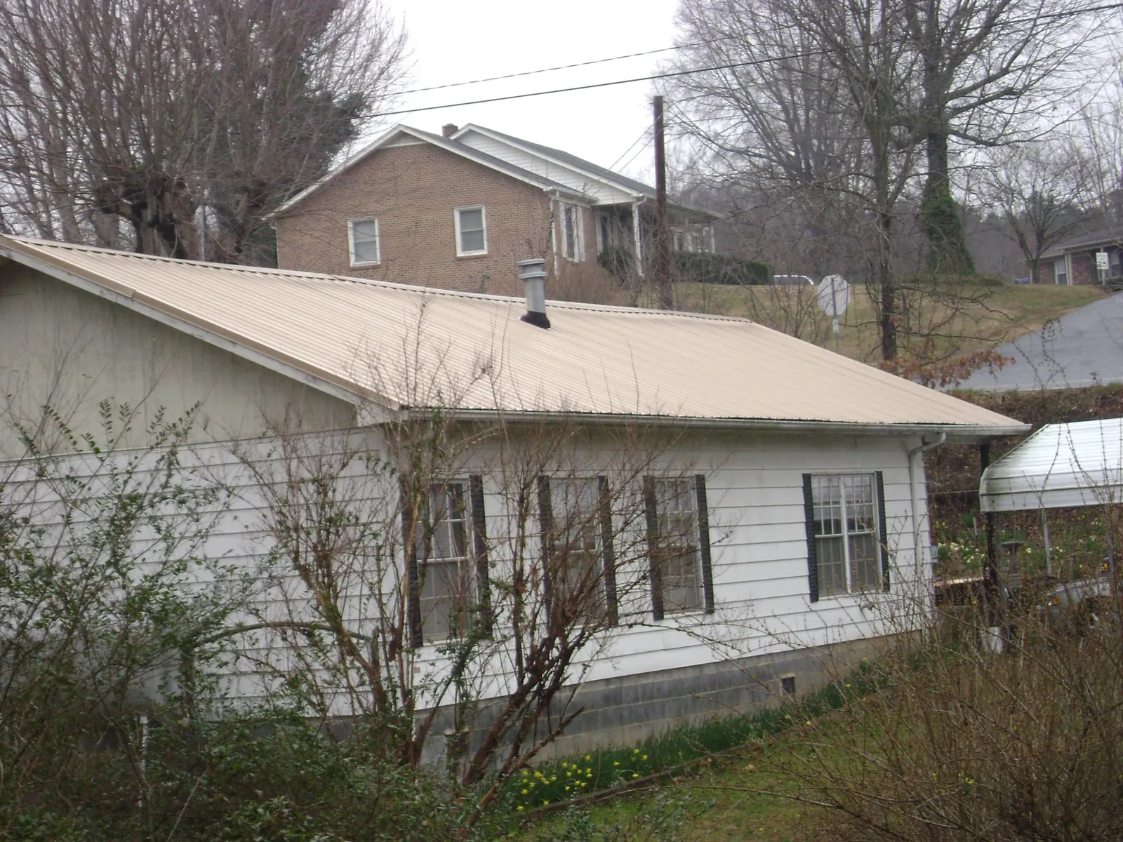 Tan metal roof on a white sided house set into a hillside — Commercial Roofing by Roofing Brothers in Bala Cynwyd